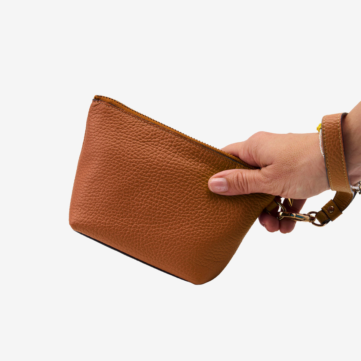 Brown leather cosmetic pouch held by a hand on a white background - TOAST