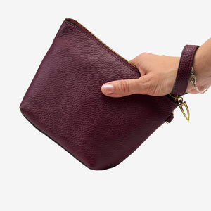 Hand holding a maroon leather clutch bag on a white background - OXBLOOD