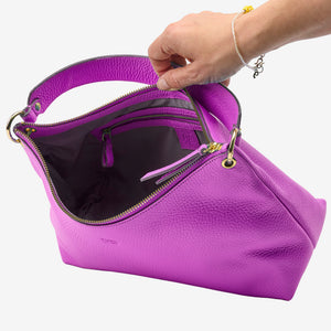 Purple handbag with gold zipper being held open by a hand on a white background - MAGENTA
