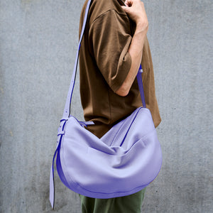 Tusk 9939 person wearing a lavender-colored leather Mira Large Hobo bag with an adjustable strap, styled against a gray concrete wall - LAVENDER