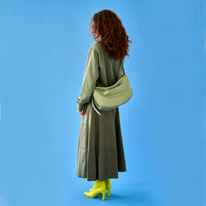 Tusk 9939 Mira Large Hobo bag in sage-colored leather, worn by a woman dressed in an olive green outfit and neon green boots, photographed from behind against a bright blue background - SAGE