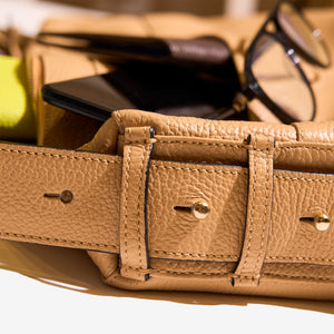 Close-up of the sand Mira Large Hobo bag  highlighting its adjustable leather strap with gold hardware, alongside partially visible contents such as glasses and a smartphone - SAND