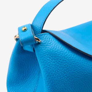 Close-up of a blue Italian leather handbag with gold hardware on a light gray background - AZURE