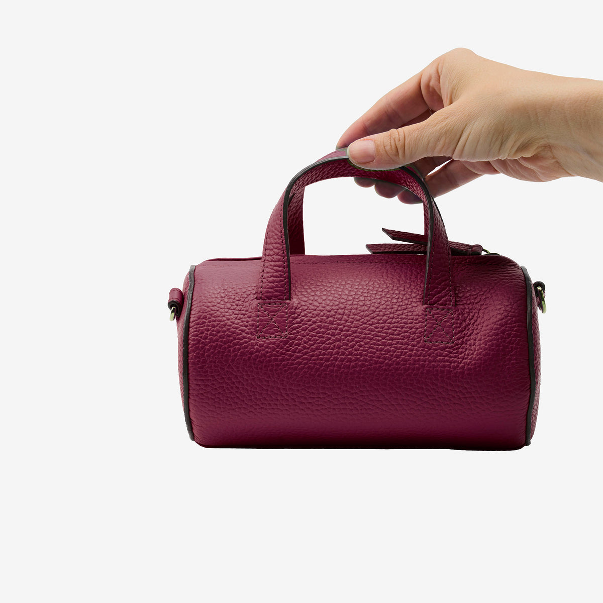 Hand holding a maroon barrel bag against a white background - OXBLOOD