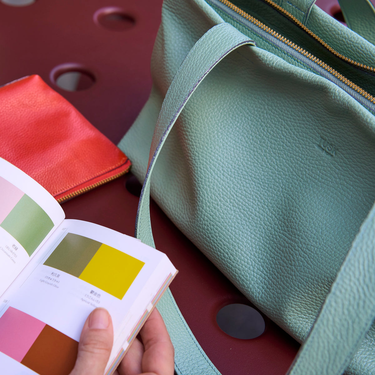 Sage green Anaya leather tote beside an orange pouch and color book - SAGE
