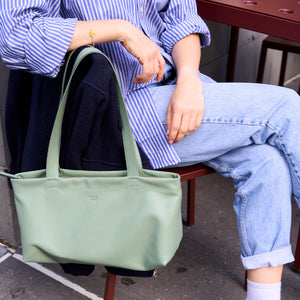 Seated model holding the sage green Anaya tote by its long handles - SAGE