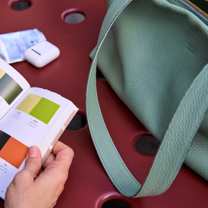 Close-up of the sage green Anaya tote's leather shoulder strap beside a color book - SAGE